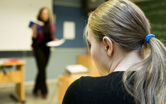 Nainen istuu luennolla, taustalla opettaja.