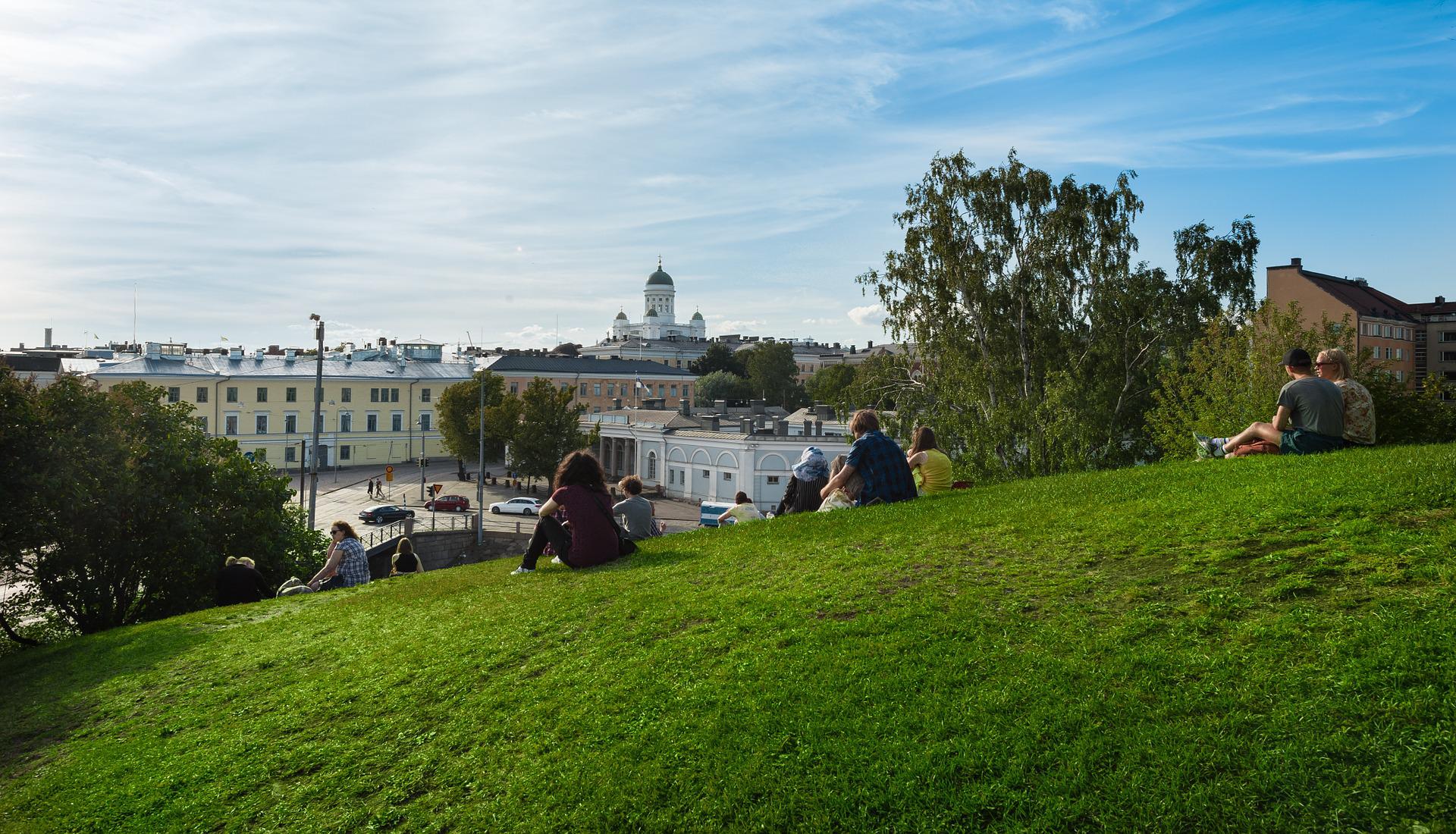 Ihmisiä istuu ruohikolla. Taustalla näkyy Helsingin tuomiokirkko.