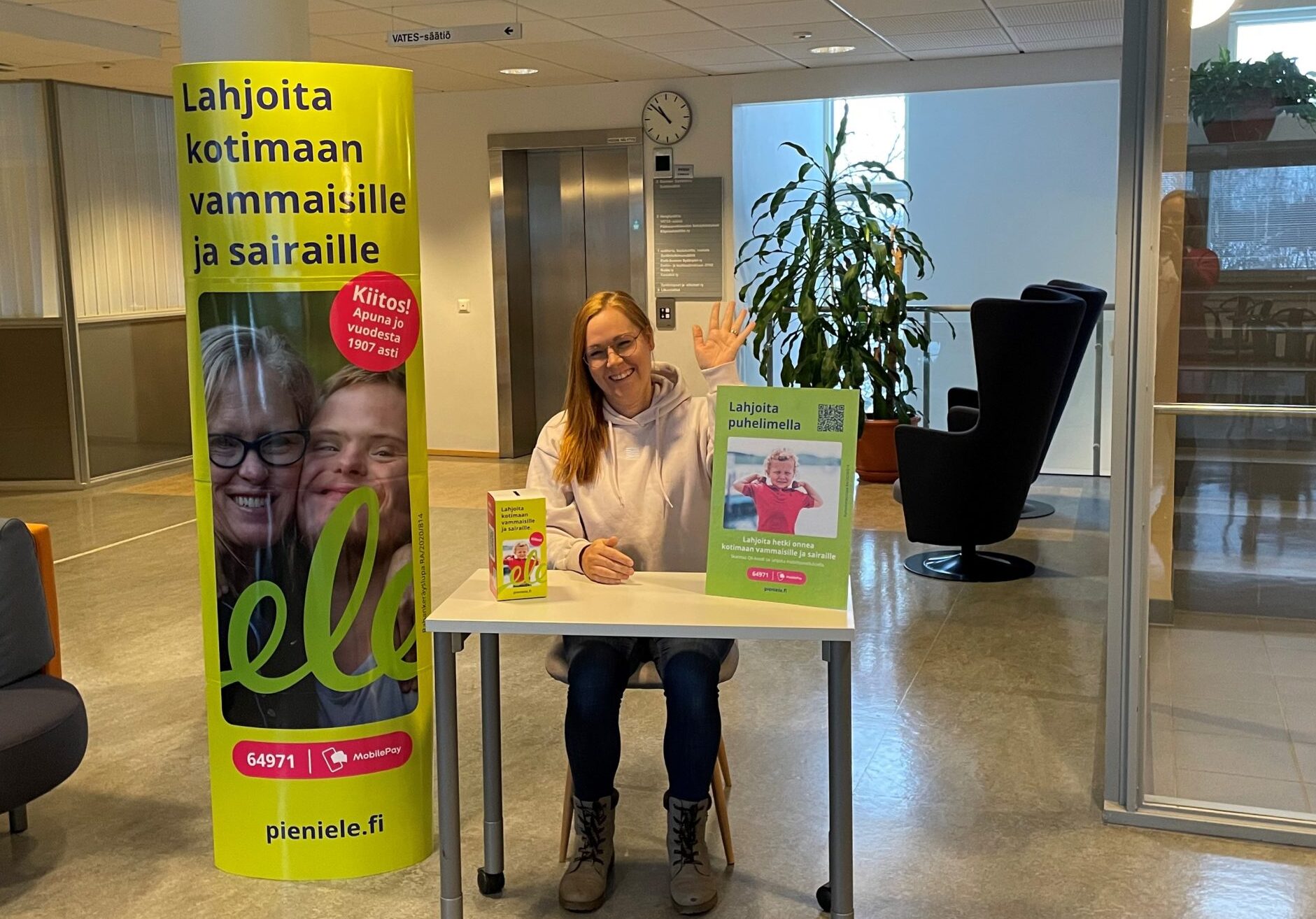 Pieni ele kerää lahjoituksia vammaisille ja pitkäaikaissairaille aluevaalien äänestyspaikoilla. Keräyspisteen iloinen vapaaehtoinen tervehtii käden heilautuksella äänestäjiä.
