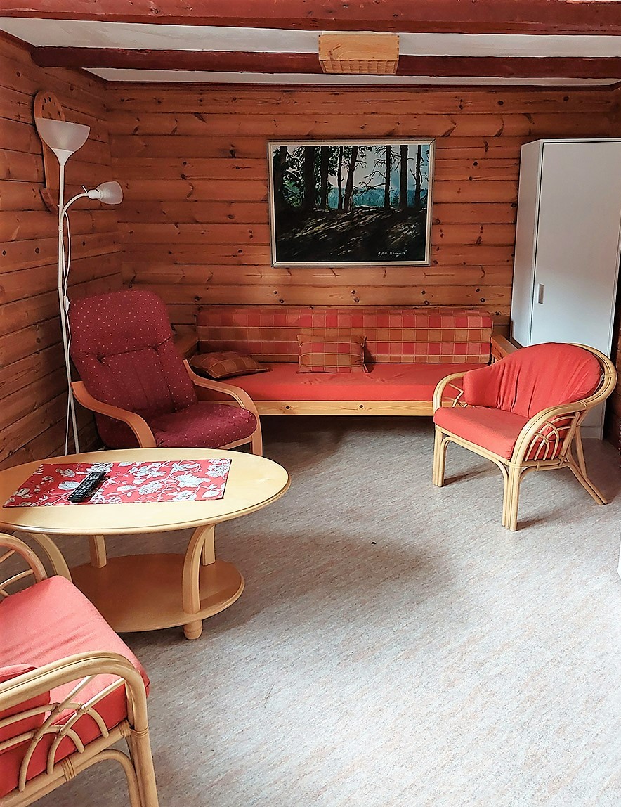 Kopolan kurssikeskuksen aitan majoitustila, jossa on pyöreä pöytä, kaksi korituolia, tv-tuoli ja vuodesohva.
