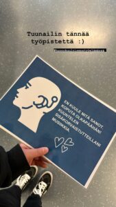 Työpisteen teksti, jossa lukee: en kuule mitä sanot, koputa olkapäähän! Kuuntelen sisäkorvaistutteillani musiikkia.