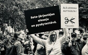 Ihmisiä järjestöjen mielenosoituksessa Esplanadin puistossa Helsingissä. Kuuloliiton toiminnanjohtaja Sanna Kaijanen pitelee kylttiä, jossa lukee ''Sote-järjestöjen alasajo on pysäytettävä.''