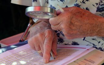 Ikäihminen lukee tekstiä suurennuslasilla.