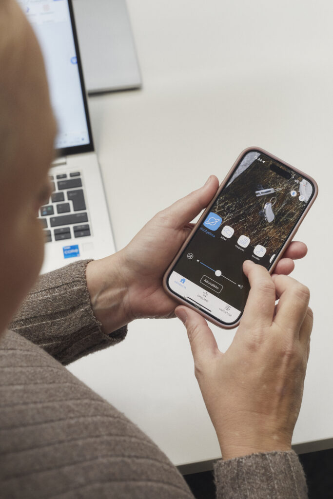 Kuvassa puhelin naisen kädessä, jossa kuulokojeen sovellus auki.