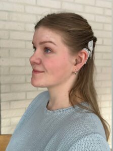 Kuva Susannasta, joka seisoo sivuttain ja hymyilee. Kuvassa näkyy audioprosessori.